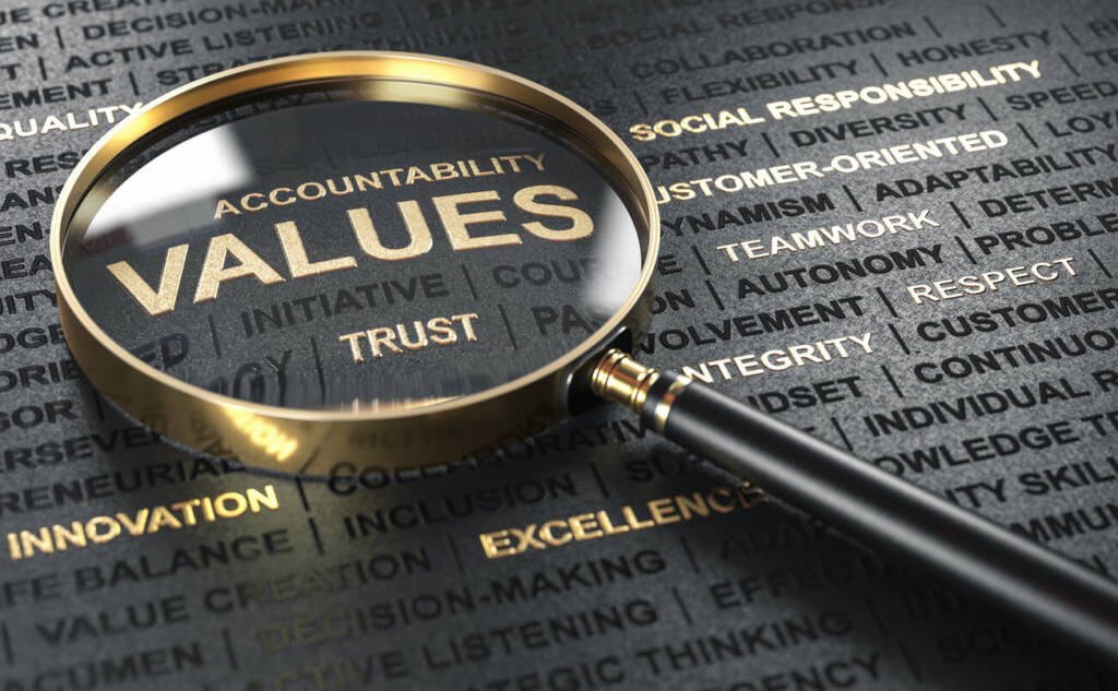 a black and gold magnifying glass sits on top of black paper with the words "accountability" and "values" being magnified under the glass.