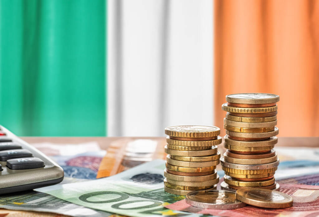 stacks of gold coins in the foreground with the irish flag in the background